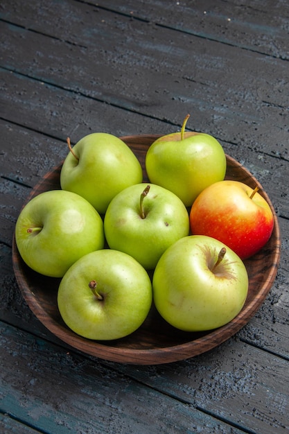 Seitenansicht aus der Ferne grün-gelb-rötliche Äpfel Holzschale mit grün-gelb-rötlichen Äpfeln auf dem grauen Tisch