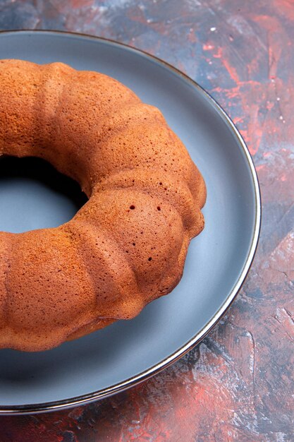 Kostenloses Foto seitenansicht aus der ferne kuchen ein appetitlicher runder kuchen auf dem teller auf dem blau-roten tisch