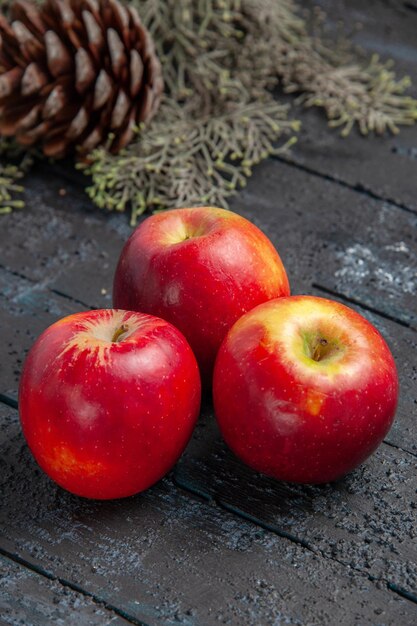 Seitenansicht aus der Ferne Äpfel auf dem Tisch drei gelb-rote Äpfel auf dem grauen Tisch mit Zweigen mit Kegel