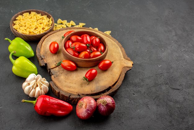 Seitenansicht aus der Ferne Schüssel auf dem Brett Schüssel mit appetitlichen Tomaten auf dem Schneidebrett neben dem Teller mit Nudeln Paprika und Knoblauch auf dem Tisch