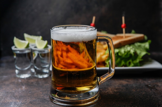 Seitenansicht Bier mit einem Teller Sandwich und Bratkartoffeln und Tequila in einem Glas mit Limetten und Salz serviert