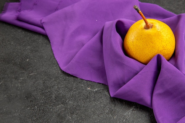 Seitenansicht Birne auf der Tischdecke gelbe Birne auf der lila Tischdecke auf dem dunklen Tisch