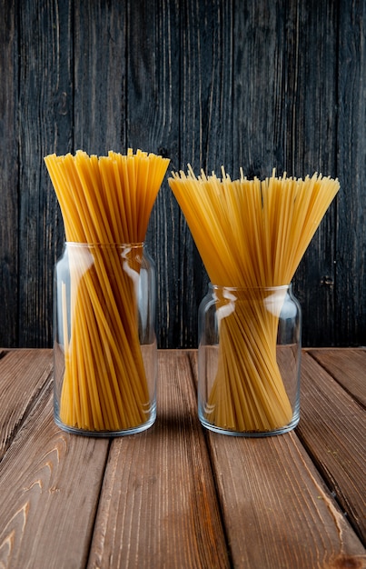 Kostenloses Foto seitenansicht bucatini und spaghetti-nudeln in einem glas auf hölzernem hintergrund