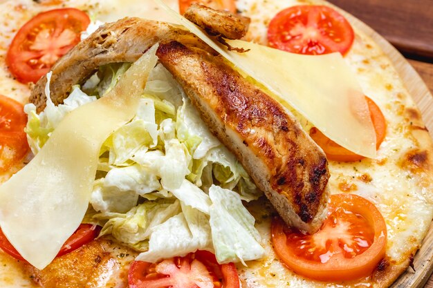 Seitenansicht Caesar Pizza mit gegrilltem Hühnchen Tomaten geschmolzenem Käse Parmesan und Salat auf einem Brett