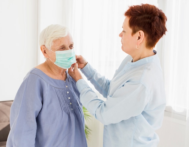 Seitenansicht der älteren Frau, die medizinische Maske auf eine andere ältere Frau setzt