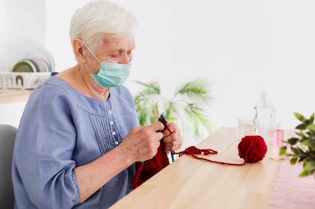 Seitenansicht der älteren Frau mit der medizinischen Maske, die zu Hause strickt