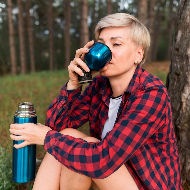 Kostenloses Foto seitenansicht der älteren touristenfrau, die aus der thermoskanne trinkt