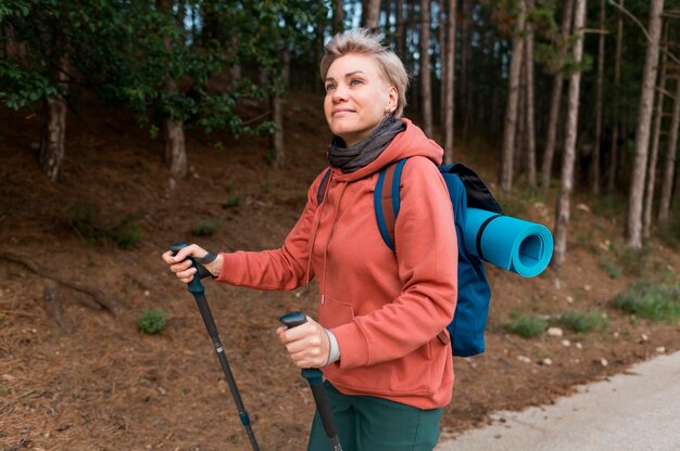 Seitenansicht der älteren Touristenfrau im Wald mit Wanderstöcken