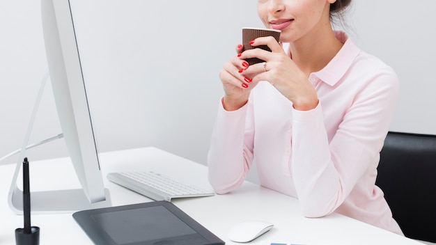 Seitenansicht der berufstätigen Frau am Schreibtisch, der Tasse Kaffee hält