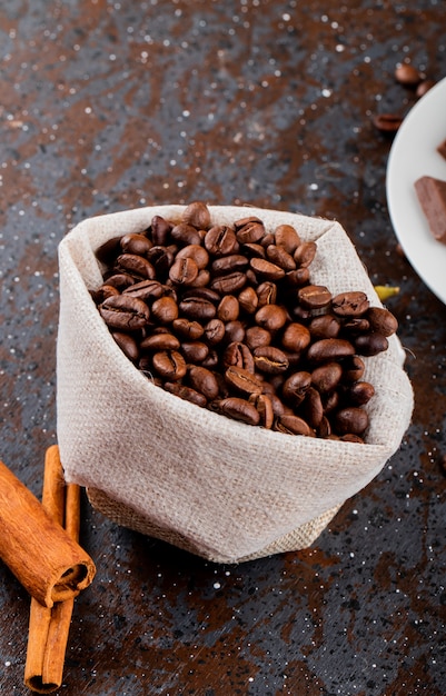 Kostenloses Foto seitenansicht der braunen kaffeebohnen in einem sack und in den zimtstangen auf schwarzem hintergrund