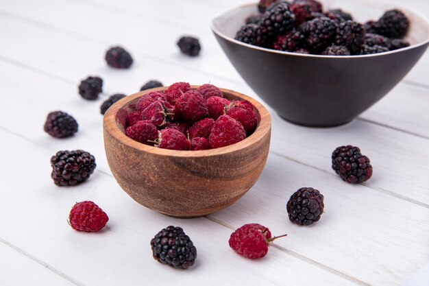 Seitenansicht der Brombeere in einer Schüssel mit Himbeeren auf einer weißen Oberfläche