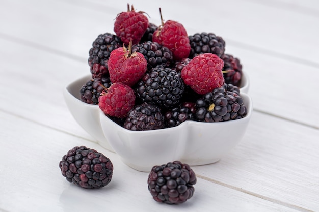 Kostenloses Foto seitenansicht der brombeere mit himbeeren in einer schüssel auf einer weißen oberfläche