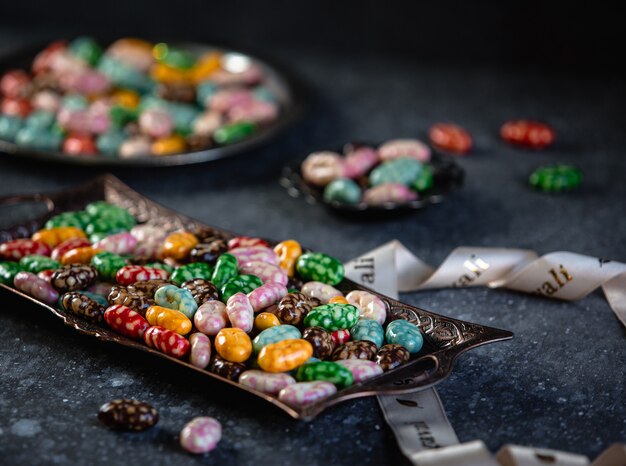 Seitenansicht der bunten glasierten Bonbons auf einem Tablett auf schwarzem Tisch