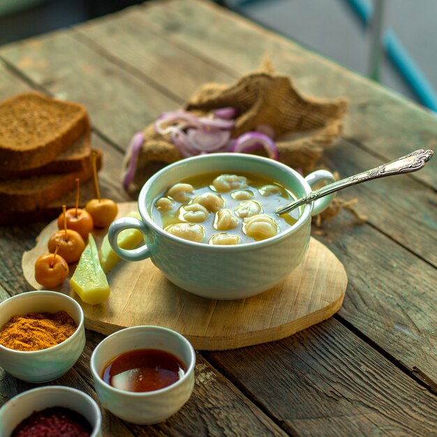 Seitenansicht der Dushbara-Knödelsuppe in der weißen Schüssel, die mit Gurken serviert wird