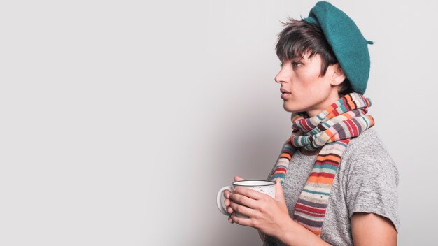 Seitenansicht der ernsten jungen Frau, die Kaffeetasse gegen grauen Hintergrund hält