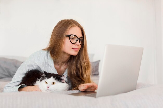 Seitenansicht der Frau, die am Laptop von zu Hause im Schlafanzug mit Katze arbeitet