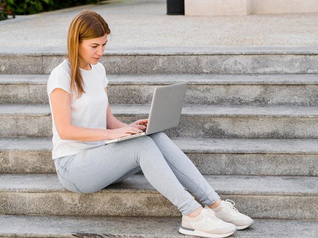 Seitenansicht der Frau, die auf Laptop im Freien auf Stufen arbeitet