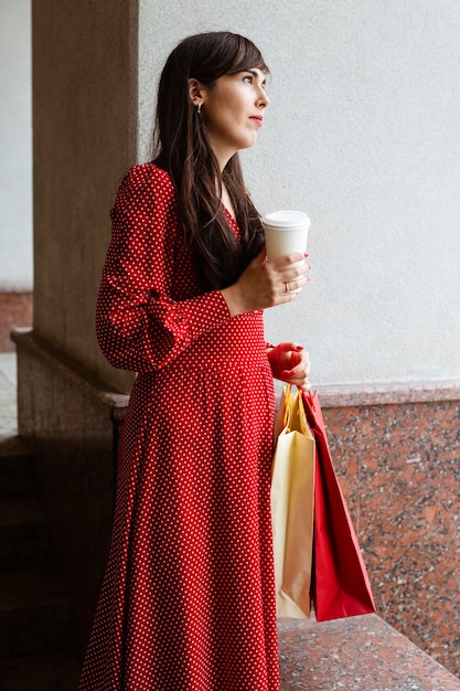 Seitenansicht der Frau, die Einkaufstaschen und Kaffee hält