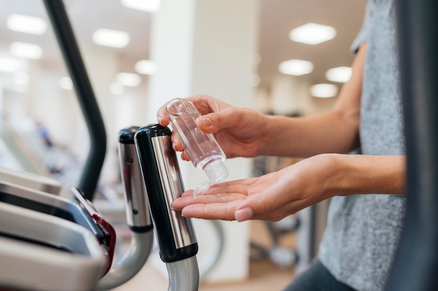 Seitenansicht der Frau, die Händedesinfektionsmittel im Fitnessstudio während der Pandemie verwendet