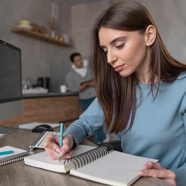 Seitenansicht der Frau, die im Medienfeld arbeitet und Sachen auf Notizbuch schreibt