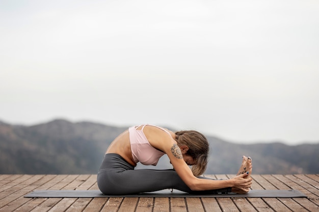 Seitenansicht der Frau, die Yoga draußen auf Matte tut