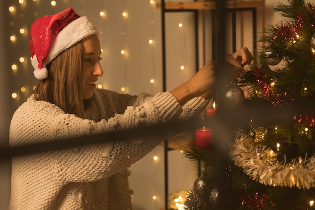 Kostenloses Foto seitenansicht der frau durch fenster, das weihnachtsbaum verziert