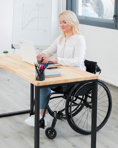 Seitenansicht der Frau im Rollstuhl am Schreibtisch arbeiten