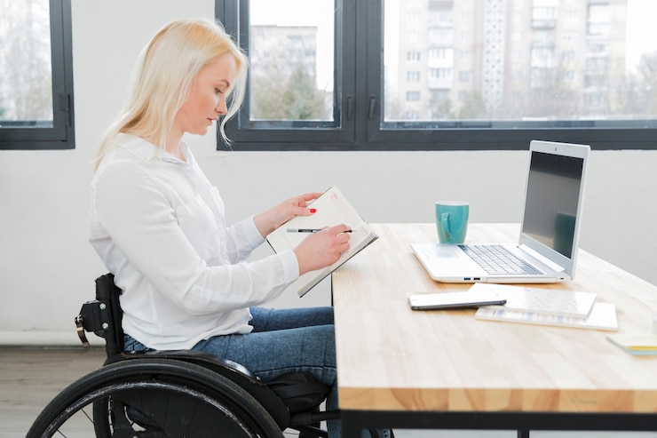 Kostenlose Foto seitenansicht der frau im rollstuhl, der am schreibtisch arbeitet