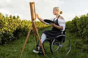 Kostenloses Foto seitenansicht der frau im rollstuhl mit palette und leinwand