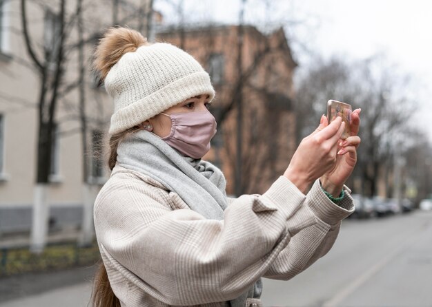 Seitenansicht der Frau mit der medizinischen Maske, die einen Videoanruf im Freien hat