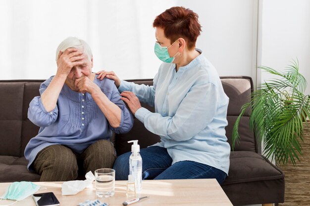 Seitenansicht der Frau mit der medizinischen Maske, die sich zu Hause um eine ältere Frau kümmert