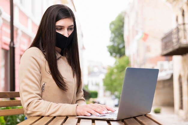 Seitenansicht der Frau mit Gesichtsmaske, die auf Laptop im Freien arbeitet