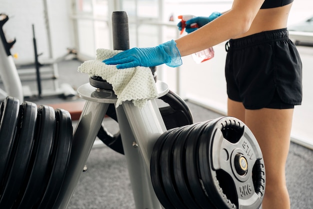 Seitenansicht der Frau mit Handschuhen, die Fitnessgeräte desinfizieren