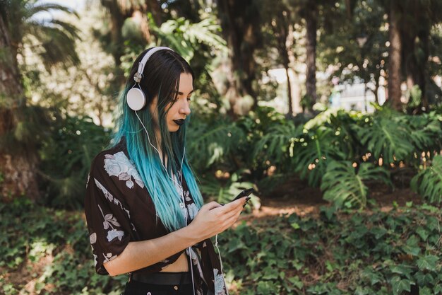 Seitenansicht der Frau mit hörender Musik des gefärbten Haares auf Kopfhörer unter Verwendung des intelligenten Telefons
