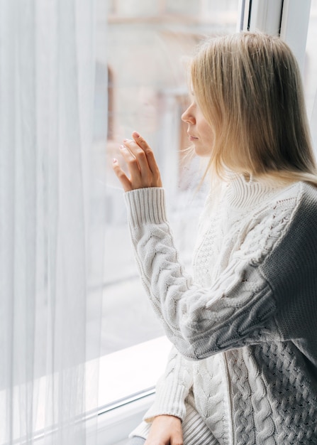 Seitenansicht der Frau zu Hause während der Pandemie, die durch das Fenster schaut