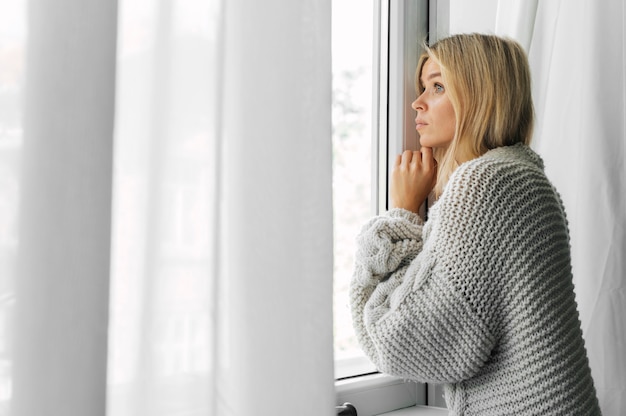 Seitenansicht der Frau zu Hause während der Pandemie, die durch das Fenster späht