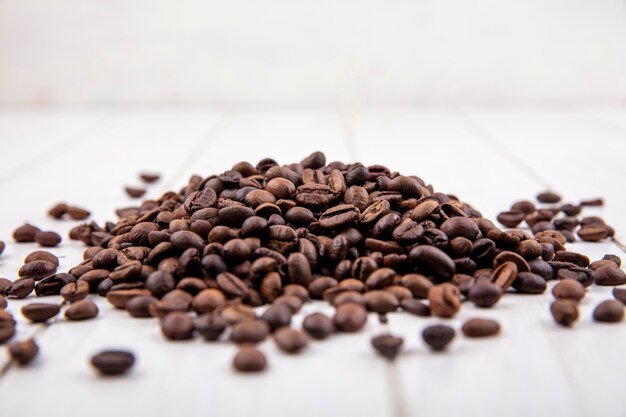 Seitenansicht der frischen Kaffeebohnen lokalisiert auf einem weißen hölzernen Hintergrund