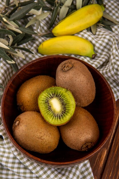 Seitenansicht der frischen Kiwi in einer Holzschale mit Bananen auf karierter Tischdecke