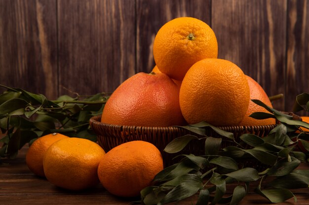 Seitenansicht der frischen reifen Orangen in einem Weidenkorb und in den grünen Blättern auf dunklem Holz