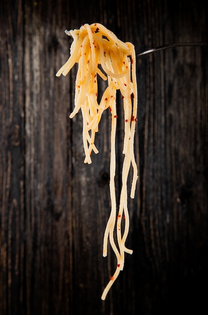 Seitenansicht der Gabel mit Spaghetti mit Chiliflocken im Dunkeln