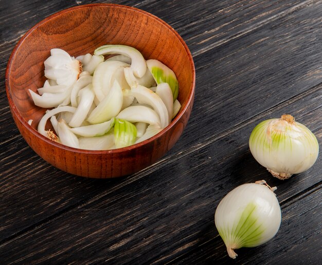 Seitenansicht der geschnittenen weißen Zwiebel in der Schüssel mit ganzen auf Holztisch