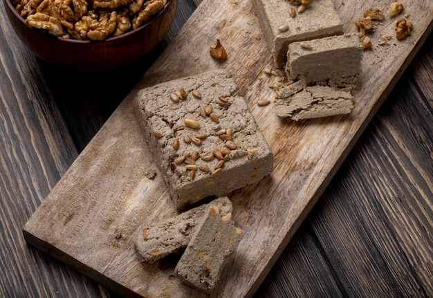 Seitenansicht der Halva mit Sonnenblumenkernen auf einem Holzbrett und einer Schüssel Walnüssen auf rustikalem