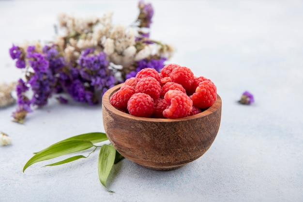 Seitenansicht der Himbeeren in der Schüssel mit Blumen und Blättern auf Weiß