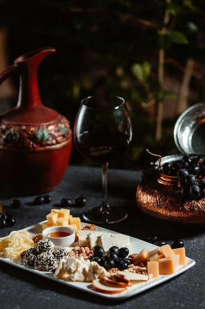 Seitenansicht der Käseplatte serviert mit Traube und Honig auf schwarzem Tisch