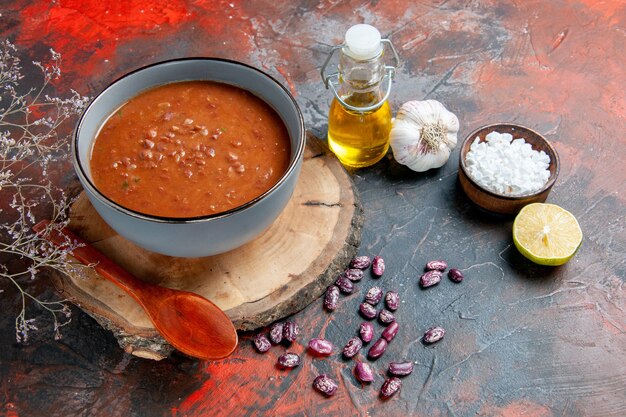 Seitenansicht der klassischen Tomatensuppe in einem blauen Schüssellöffel auf Holztablettölflasche Knoblauchsalz und Zitrone auf Mischfarbtabelle