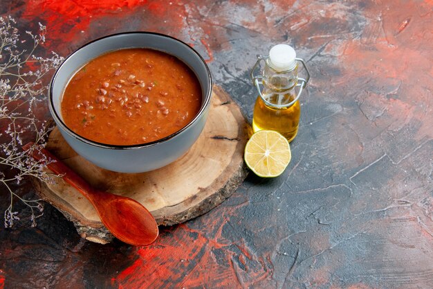 Seitenansicht der klassischen Tomatensuppe in einer blauen Schüssel auf Holztablettölflasche und Zitrone auf Mischfarbtabelle