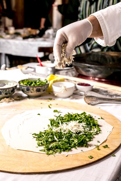 Seitenansicht Der Koch kocht Cutab mit Gemüse und bestreut mit Käse auf einem Brett mit Zutaten