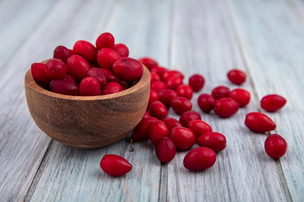 Kostenloses Foto seitenansicht der kornelkirschenbeeren in der schüssel und auf hölzernem hintergrund