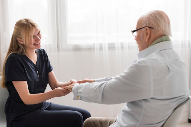 Seitenansicht der Krankenschwester, die die Hände des älteren Mannes hält