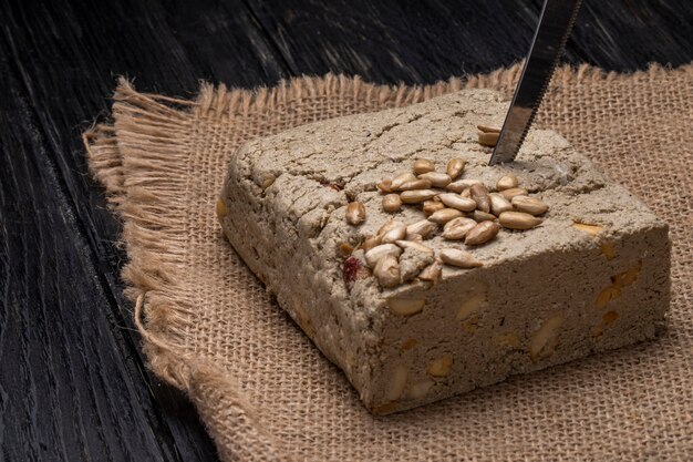 Seitenansicht der leckeren Halva mit einem Messer und Sonnenblumenkernen auf einem Sack